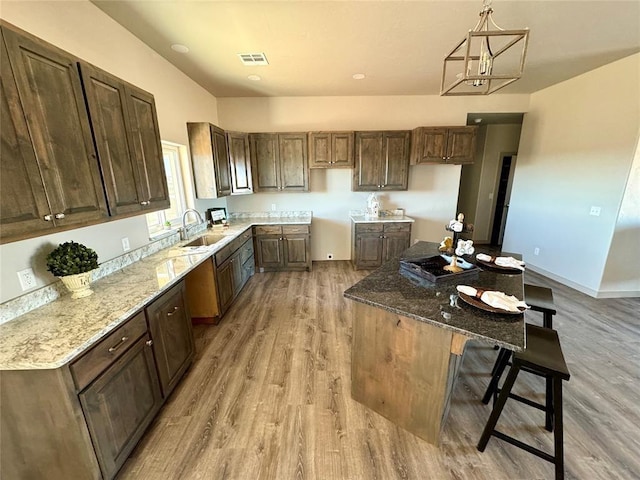 kitchen featuring sink, a kitchen breakfast bar, light stone counters, pendant lighting, and light hardwood / wood-style floors