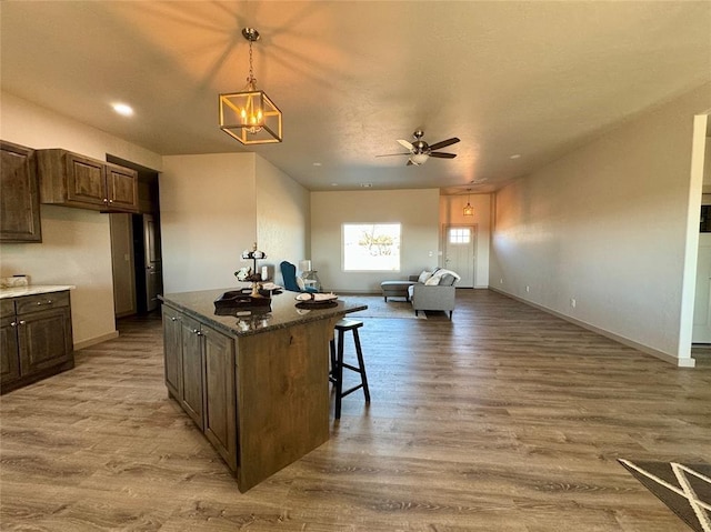 kitchen featuring ceiling fan, a center island, a kitchen breakfast bar, hardwood / wood-style floors, and decorative light fixtures