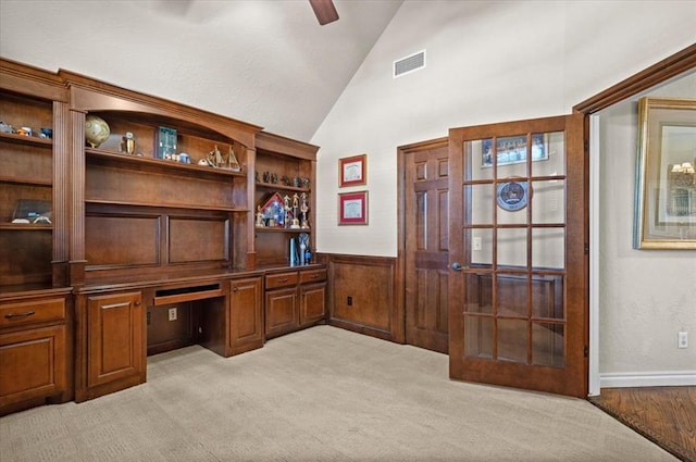 carpeted office with lofted ceiling, built in desk, ceiling fan, and wood walls