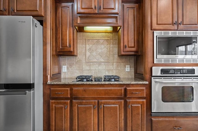 kitchen with stainless steel appliances, tasteful backsplash, brown cabinetry, and light stone countertops