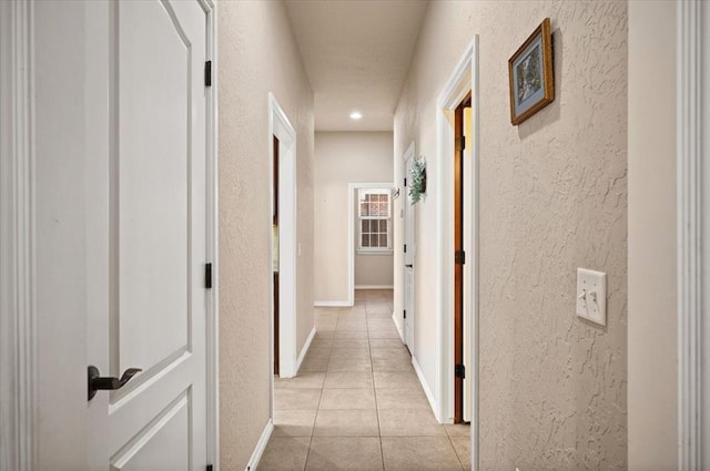 corridor featuring recessed lighting, light tile patterned flooring, a textured wall, and baseboards