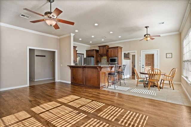 kitchen with a breakfast bar, crown molding, light wood finished floors, appliances with stainless steel finishes, and a peninsula