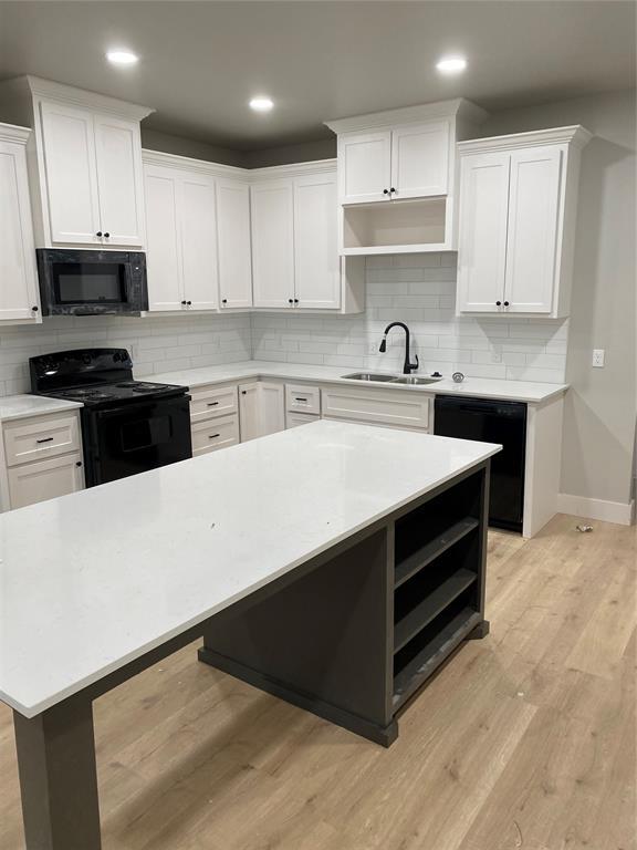 kitchen with a kitchen island, sink, white cabinets, black appliances, and light wood-type flooring