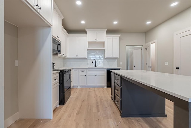 kitchen with light wood-type flooring, black appliances, white cabinets, light stone countertops, and tasteful backsplash