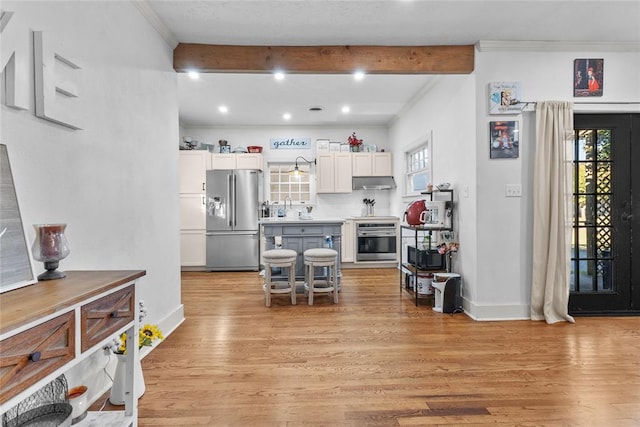 kitchen with beam ceiling, stainless steel appliances, light hardwood / wood-style flooring, and a wealth of natural light