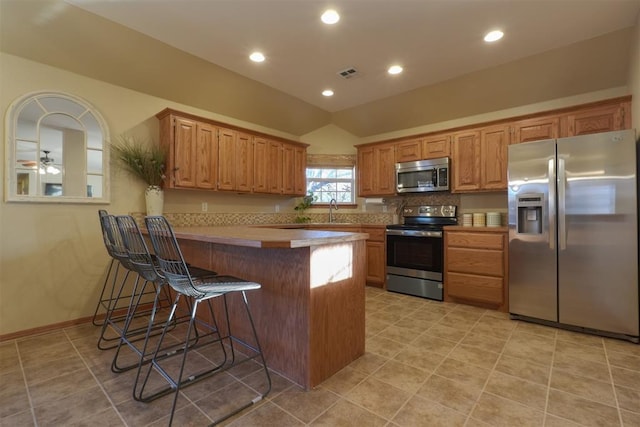 kitchen with ceiling fan, stainless steel appliances, kitchen peninsula, lofted ceiling, and a breakfast bar area