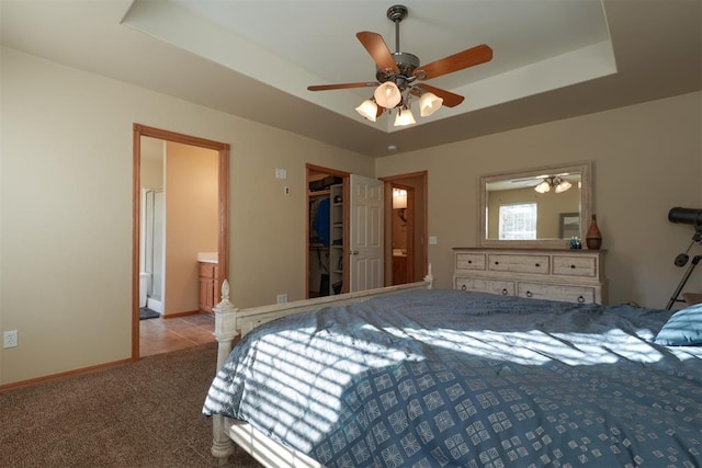 carpeted bedroom with ensuite bathroom, a raised ceiling, a walk in closet, ceiling fan, and a closet