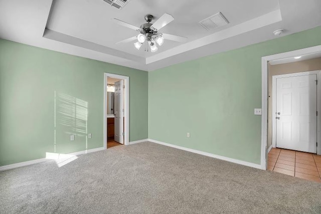 unfurnished bedroom with ceiling fan, light carpet, a tray ceiling, and ensuite bath