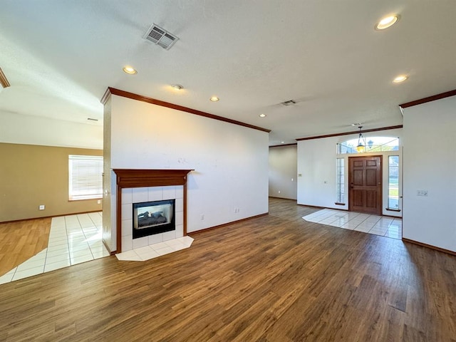 unfurnished living room featuring wood-type flooring, ornamental molding, and a tiled fireplace