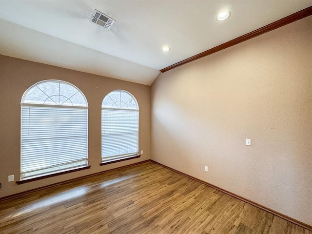 empty room with hardwood / wood-style floors, vaulted ceiling, and ornamental molding