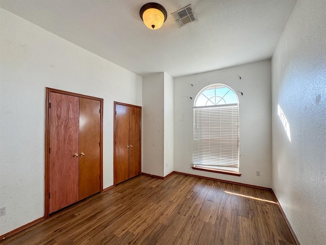 unfurnished bedroom featuring hardwood / wood-style floors and two closets