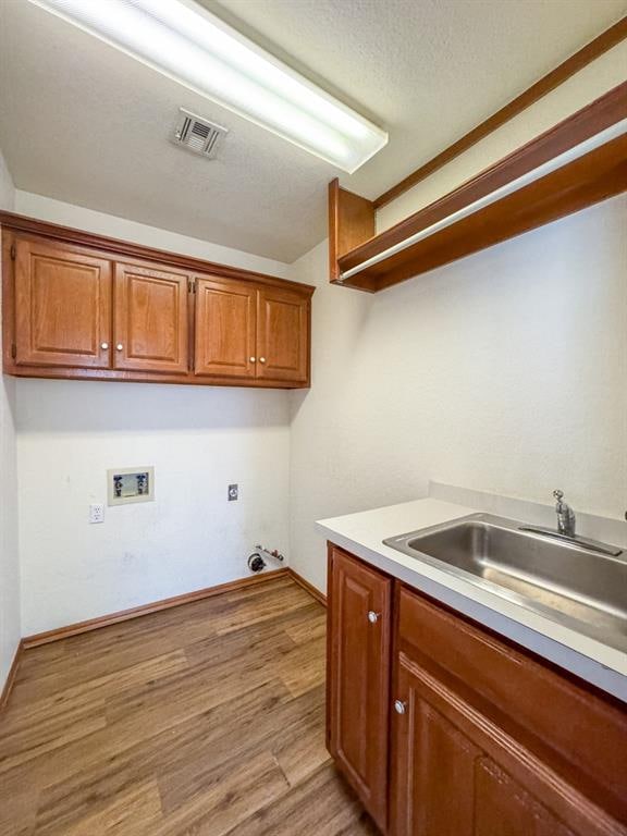 clothes washing area featuring cabinets, hookup for a washing machine, a textured ceiling, sink, and light hardwood / wood-style flooring