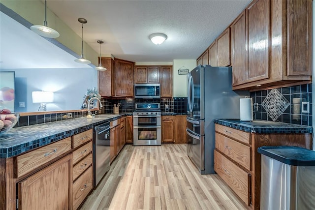 kitchen featuring stainless steel appliances, tasteful backsplash, decorative light fixtures, light wood-type flooring, and sink