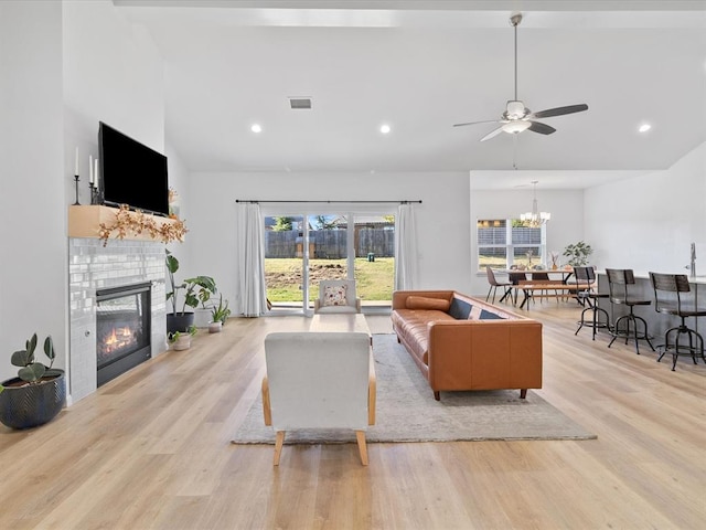 living room with ceiling fan, light wood-type flooring, plenty of natural light, and a tiled fireplace