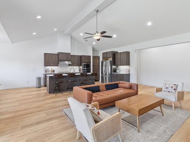 living room with high vaulted ceiling, sink, light hardwood / wood-style flooring, ceiling fan, and beam ceiling