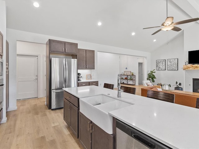 kitchen with sink, light hardwood / wood-style floors, lofted ceiling, dark brown cabinets, and appliances with stainless steel finishes