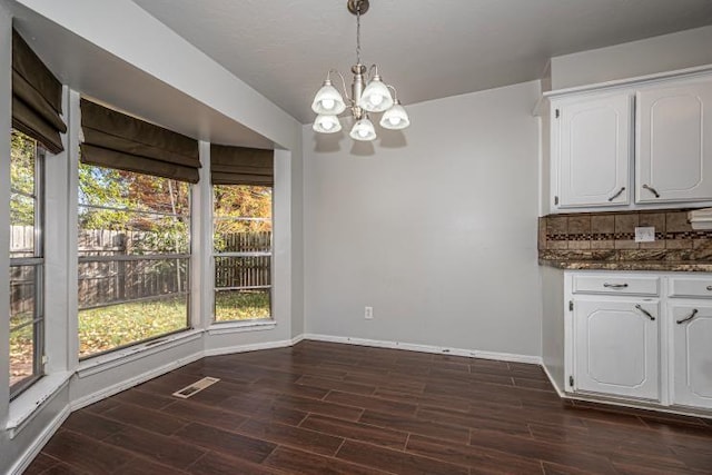 unfurnished dining area featuring plenty of natural light, dark wood-type flooring, and an inviting chandelier