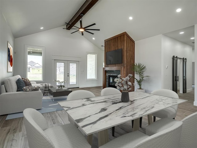 dining space featuring french doors, a barn door, light hardwood / wood-style flooring, beamed ceiling, and a fireplace