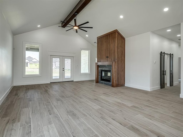 unfurnished living room with lofted ceiling with beams, light hardwood / wood-style flooring, ceiling fan, a barn door, and french doors