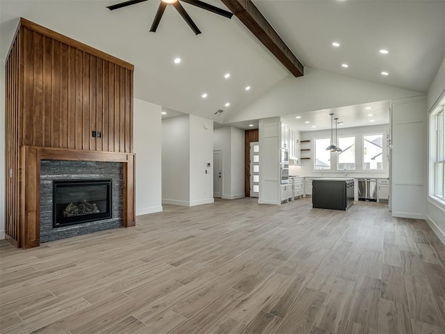 unfurnished living room featuring beam ceiling, high vaulted ceiling, ceiling fan, a fireplace, and light hardwood / wood-style floors