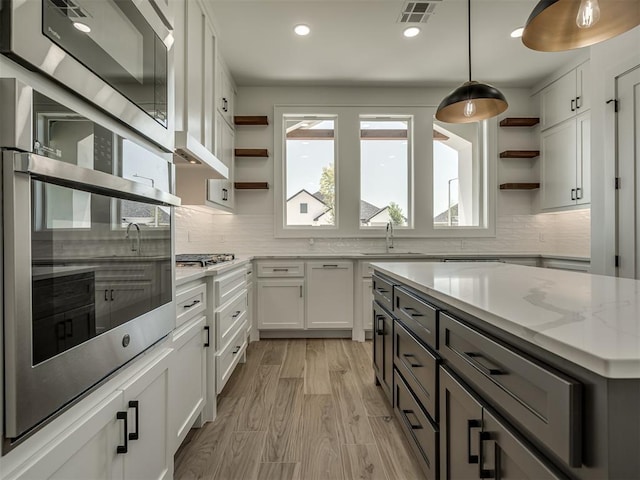 kitchen with sink, light stone counters, hanging light fixtures, stainless steel appliances, and white cabinets