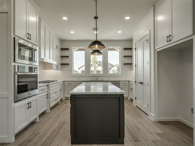 kitchen with white cabinetry, stainless steel appliances, a kitchen island, and hanging light fixtures