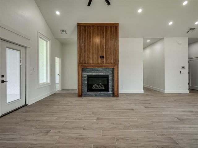 unfurnished living room featuring a stone fireplace, high vaulted ceiling, and light wood-type flooring