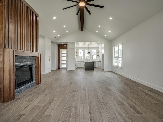 unfurnished living room with a stone fireplace, high vaulted ceiling, beamed ceiling, ceiling fan, and hardwood / wood-style floors