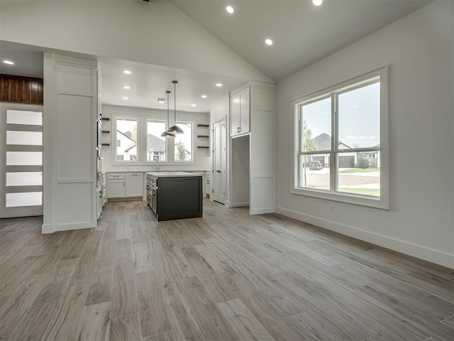 kitchen with a kitchen island, decorative light fixtures, white cabinetry, lofted ceiling, and light wood-type flooring