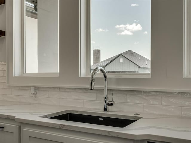 kitchen featuring light stone counters, sink, tasteful backsplash, and white cabinets