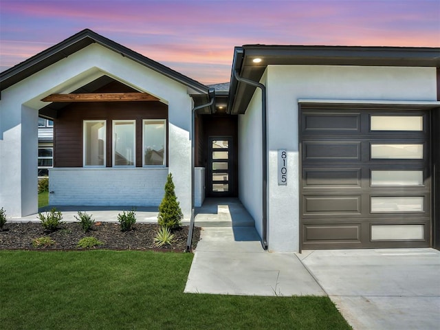 exterior entry at dusk featuring a garage and a lawn