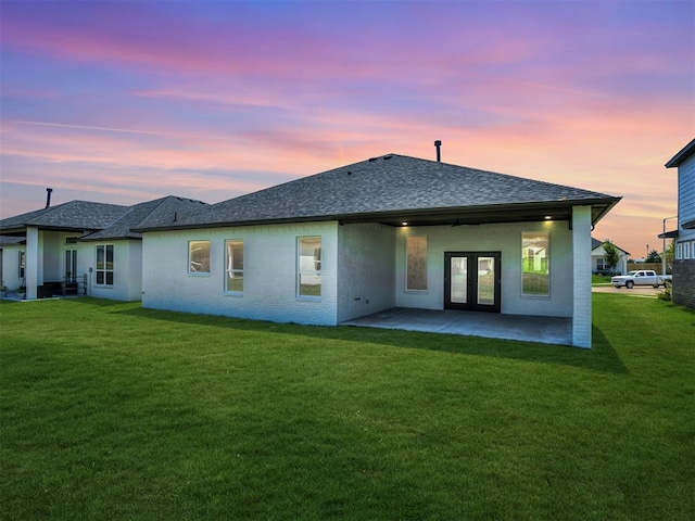 back house at dusk with a patio area and a lawn