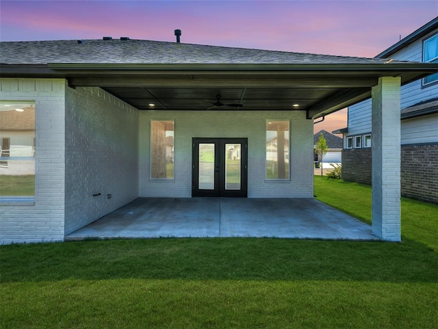 back house at dusk featuring french doors, a lawn, ceiling fan, and a patio area