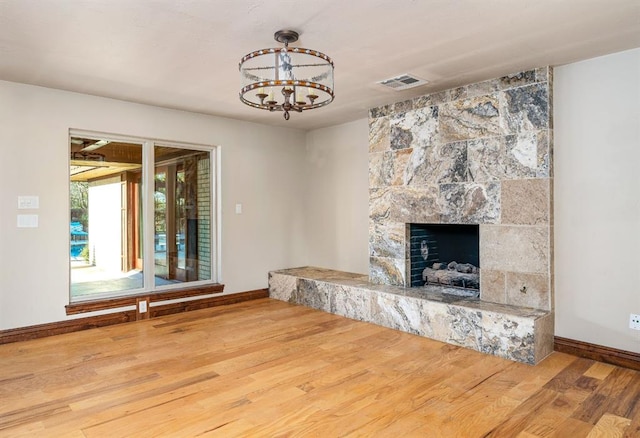 unfurnished living room featuring hardwood / wood-style floors, an inviting chandelier, and a tiled fireplace