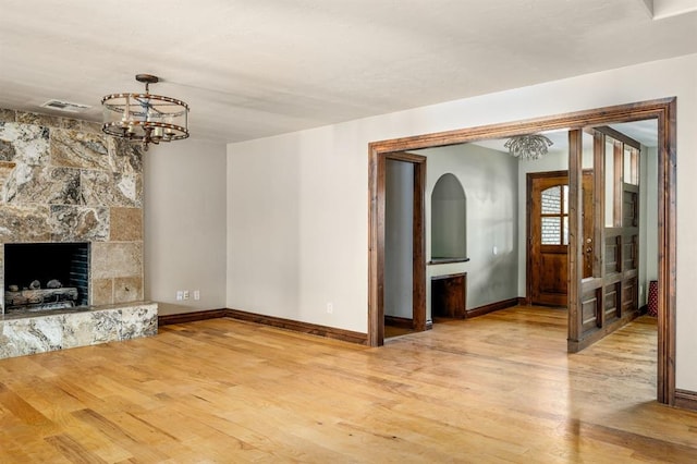 unfurnished living room with light hardwood / wood-style floors, a notable chandelier, and a fireplace