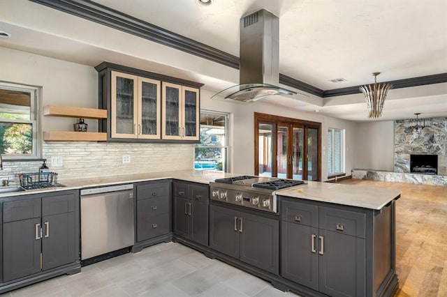 kitchen featuring pendant lighting, appliances with stainless steel finishes, island exhaust hood, a fireplace, and kitchen peninsula