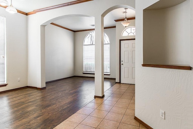 entrance foyer featuring light wood finished floors, baseboards, arched walkways, and crown molding