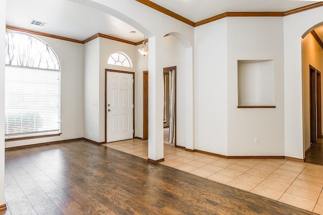 entrance foyer featuring arched walkways, crown molding, visible vents, wood finished floors, and baseboards