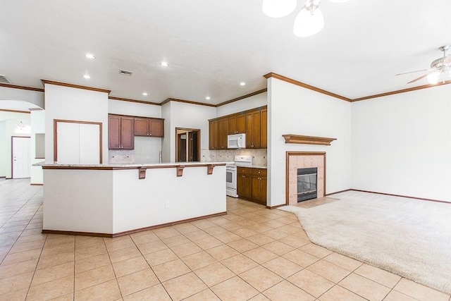 kitchen featuring ceiling fan, white appliances, a breakfast bar area, decorative backsplash, and a center island with sink