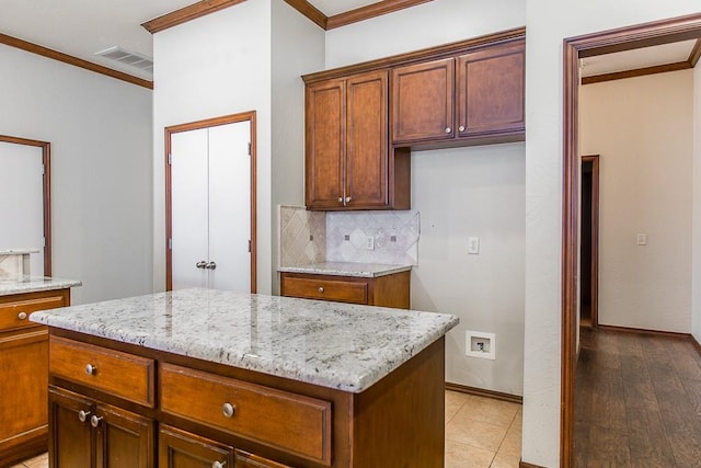 kitchen with a center island, ornamental molding, tasteful backsplash, light hardwood / wood-style floors, and light stone counters