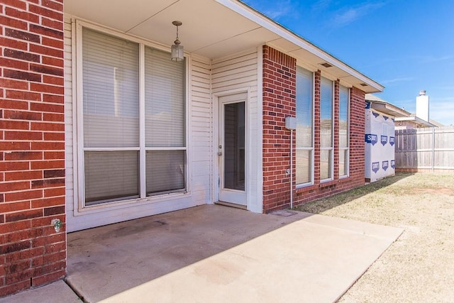 doorway to property with brick siding, fence, and a patio