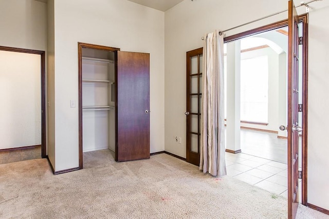 unfurnished bedroom featuring baseboards, arched walkways, tile patterned floors, carpet floors, and a closet