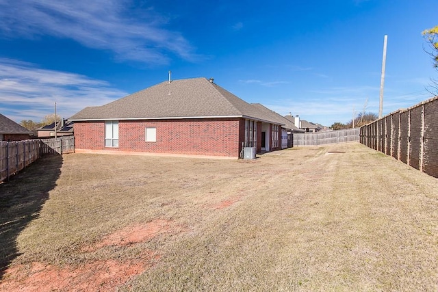 view of side of property with brick siding, a yard, a shingled roof, central AC, and a fenced backyard