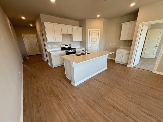 kitchen with white cabinets, a center island with sink, light wood-type flooring, and stainless steel stove