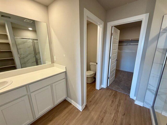 bathroom with hardwood / wood-style floors, vanity, a shower with shower door, and toilet