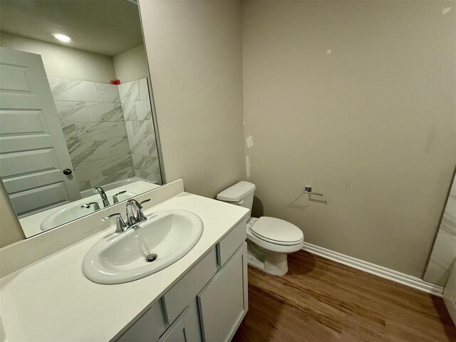 bathroom with vanity, toilet, a tile shower, and wood-type flooring