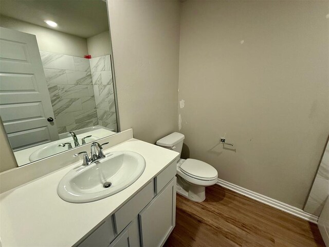 bathroom featuring toilet, hardwood / wood-style floors, vanity, and a tile shower