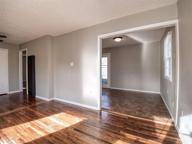 empty room with a textured ceiling, ceiling fan, and dark wood-type flooring