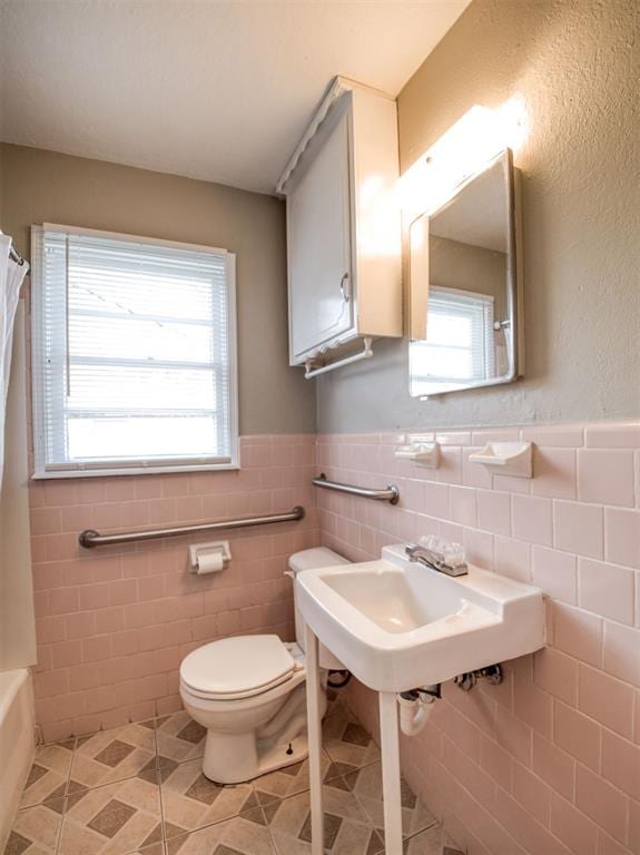 bathroom with tile patterned floors, a healthy amount of sunlight, and tile walls