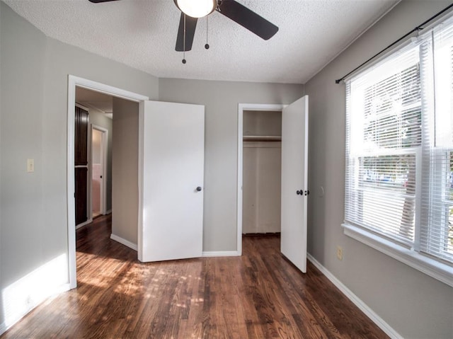 unfurnished bedroom with a textured ceiling, ceiling fan, dark wood-type flooring, and a closet